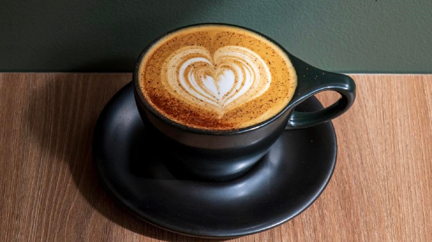 Heart-shaped latte art in black cup on saucer atop wooden table.