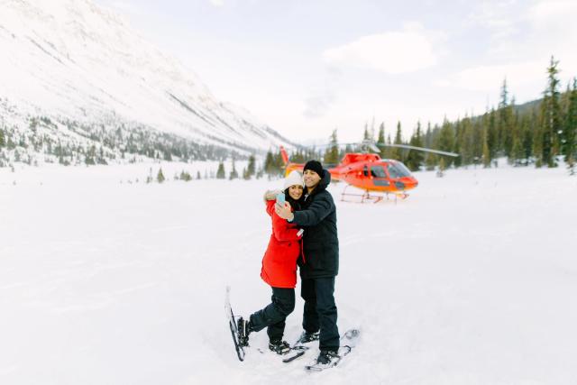 A couple heli-snowshoeing hug in front of the helicopter