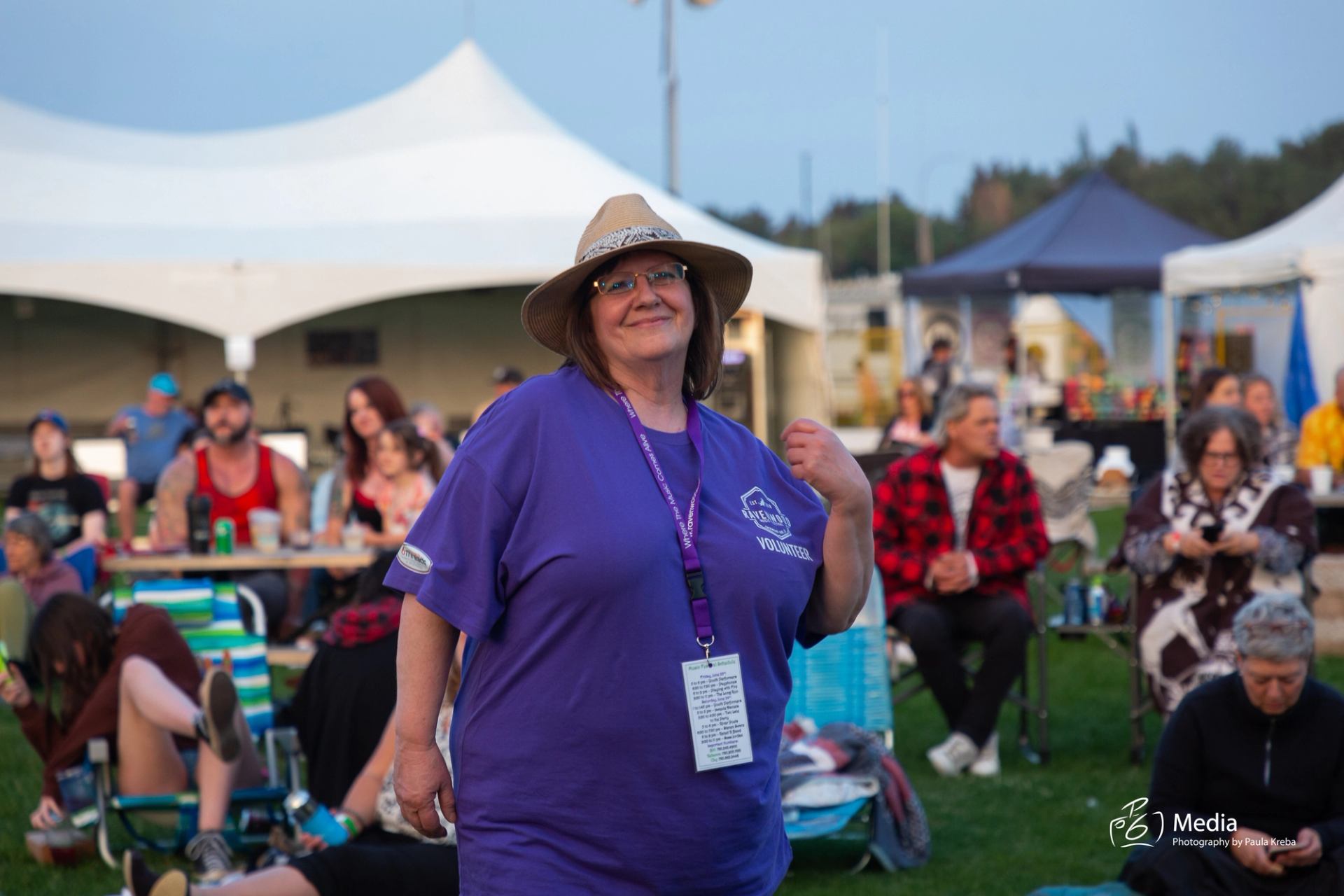 Person in purple shirt and hat walking at outdoor music festival with tents in background.
