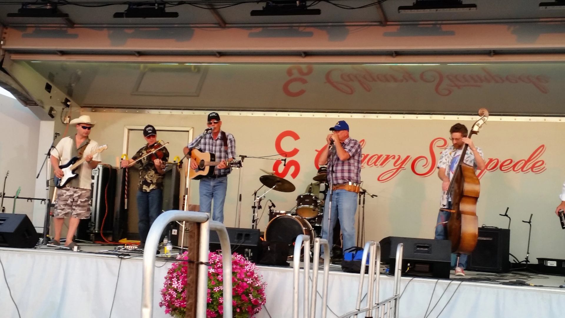 Band performing on a stage with guitars, drums and a bass, festival banner backdrop.