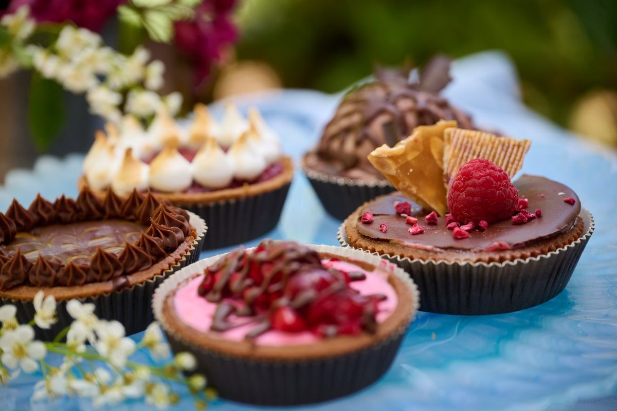 Five assorted gourmet tarts with various toppings, including raspberry, chocolate, and meringue, on a blue plate.