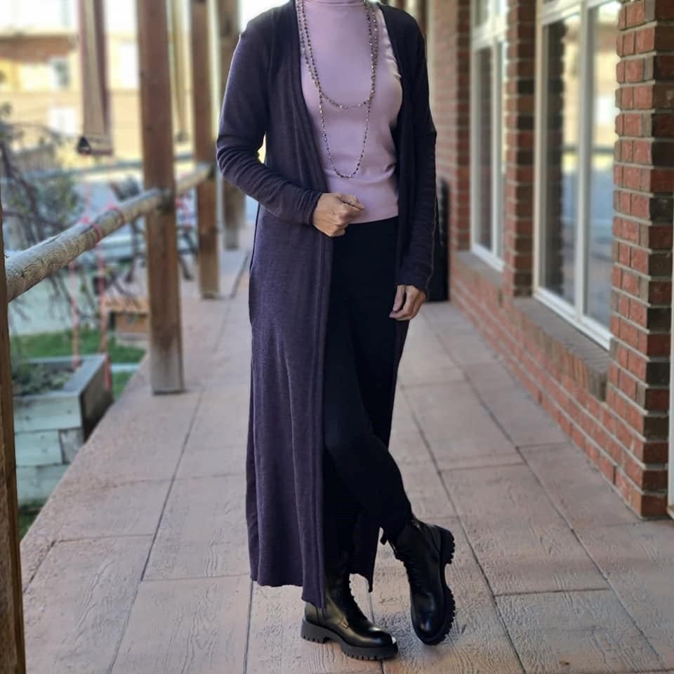 Person standing on a brick walkway, wearing a long dark cardigan and necklace.