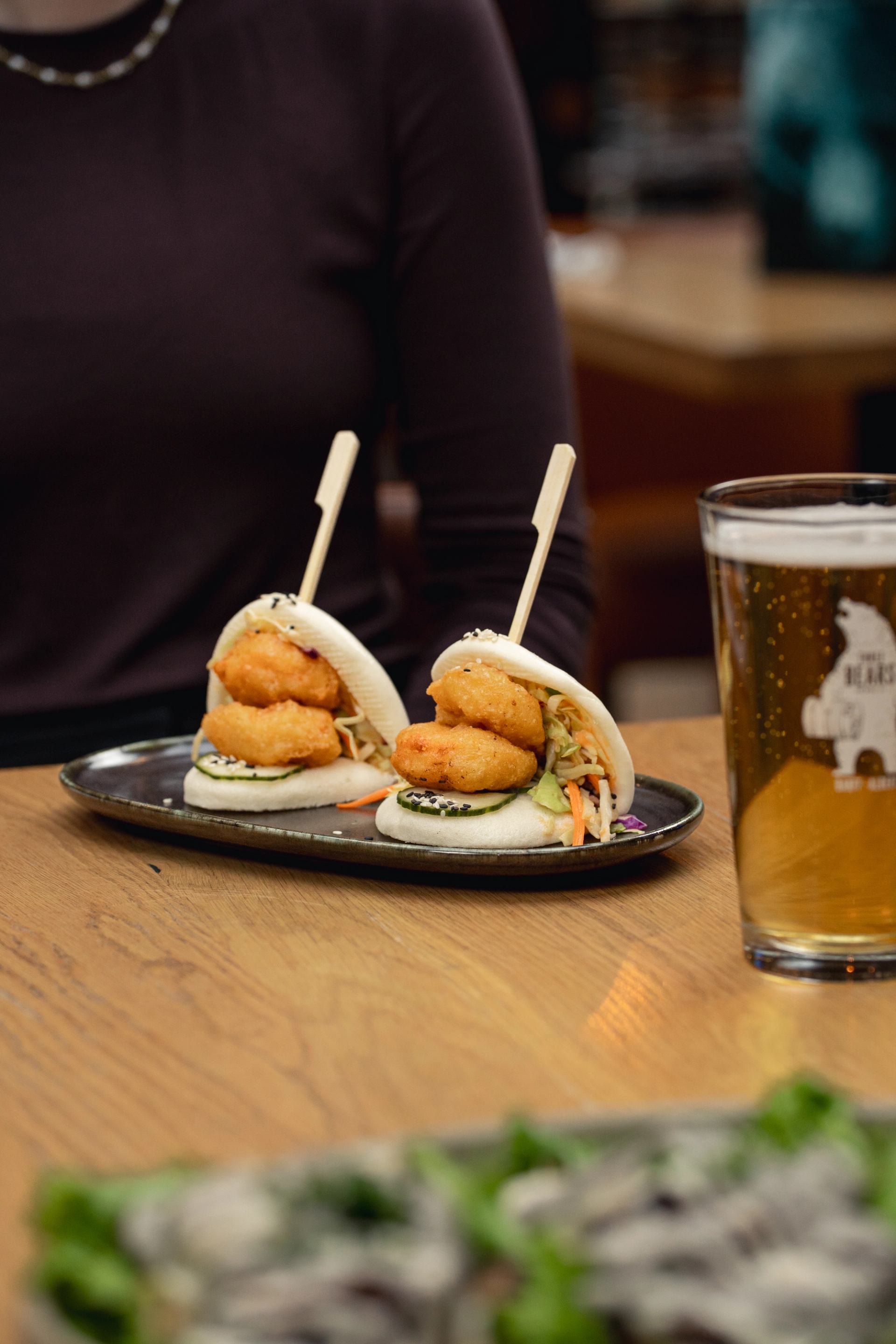 Plated deep fried shrimp on a bao bun with house pickled cucumbers, spicy mayo