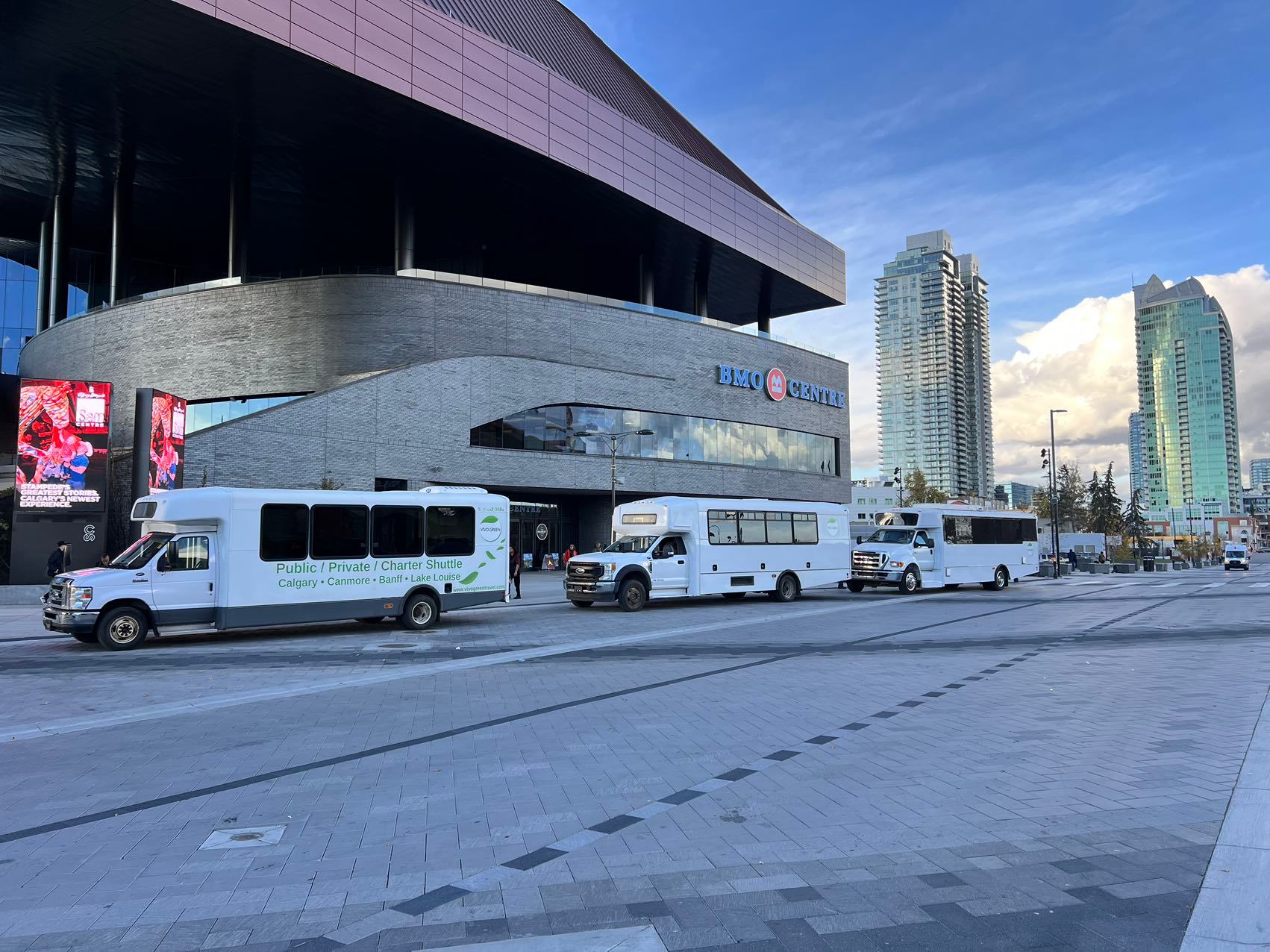 Shuttle buses line the street outside BMO Centre, with highrises in the background.
