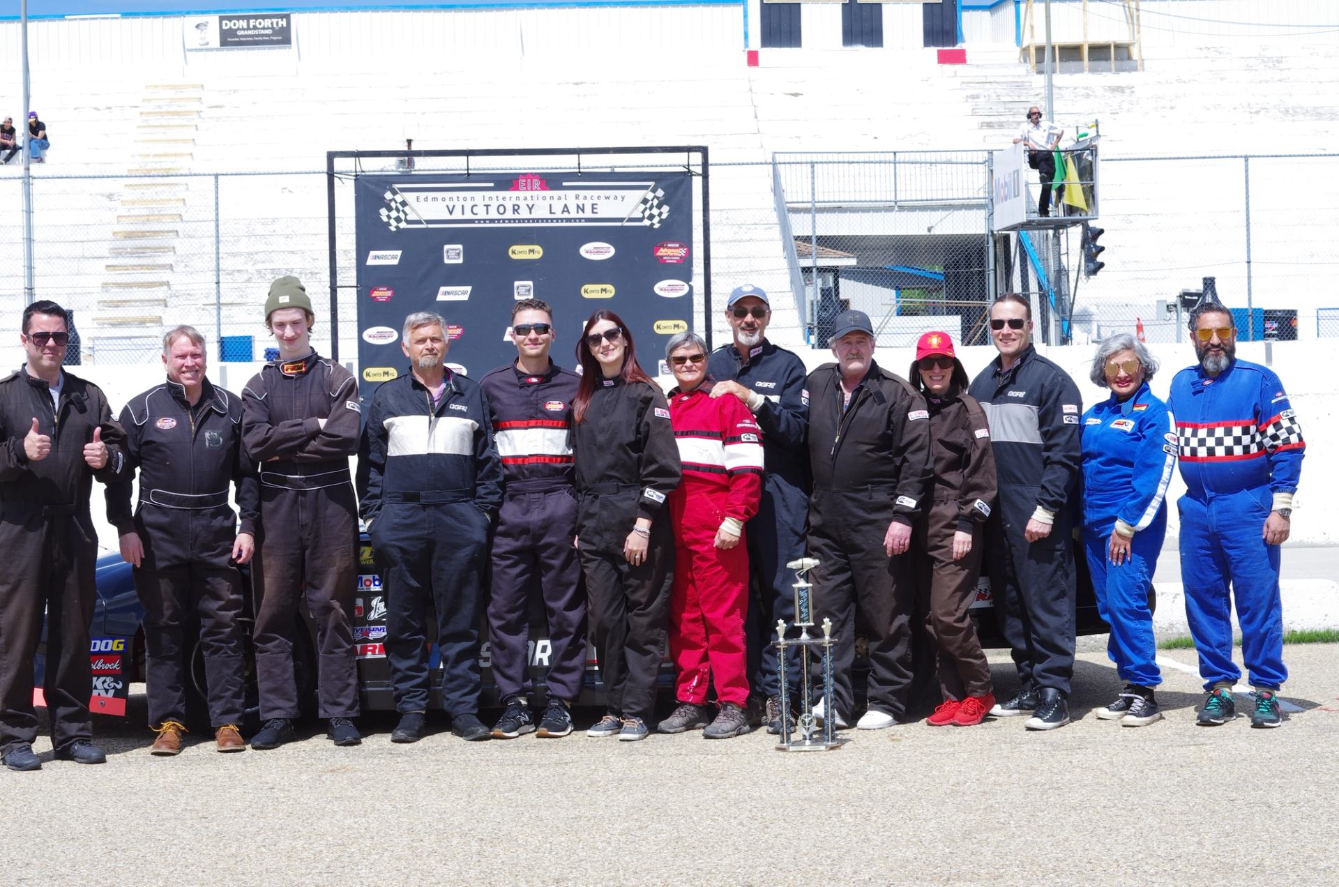 Group of people in racing suits standing by a NASCAR stock car at the track.