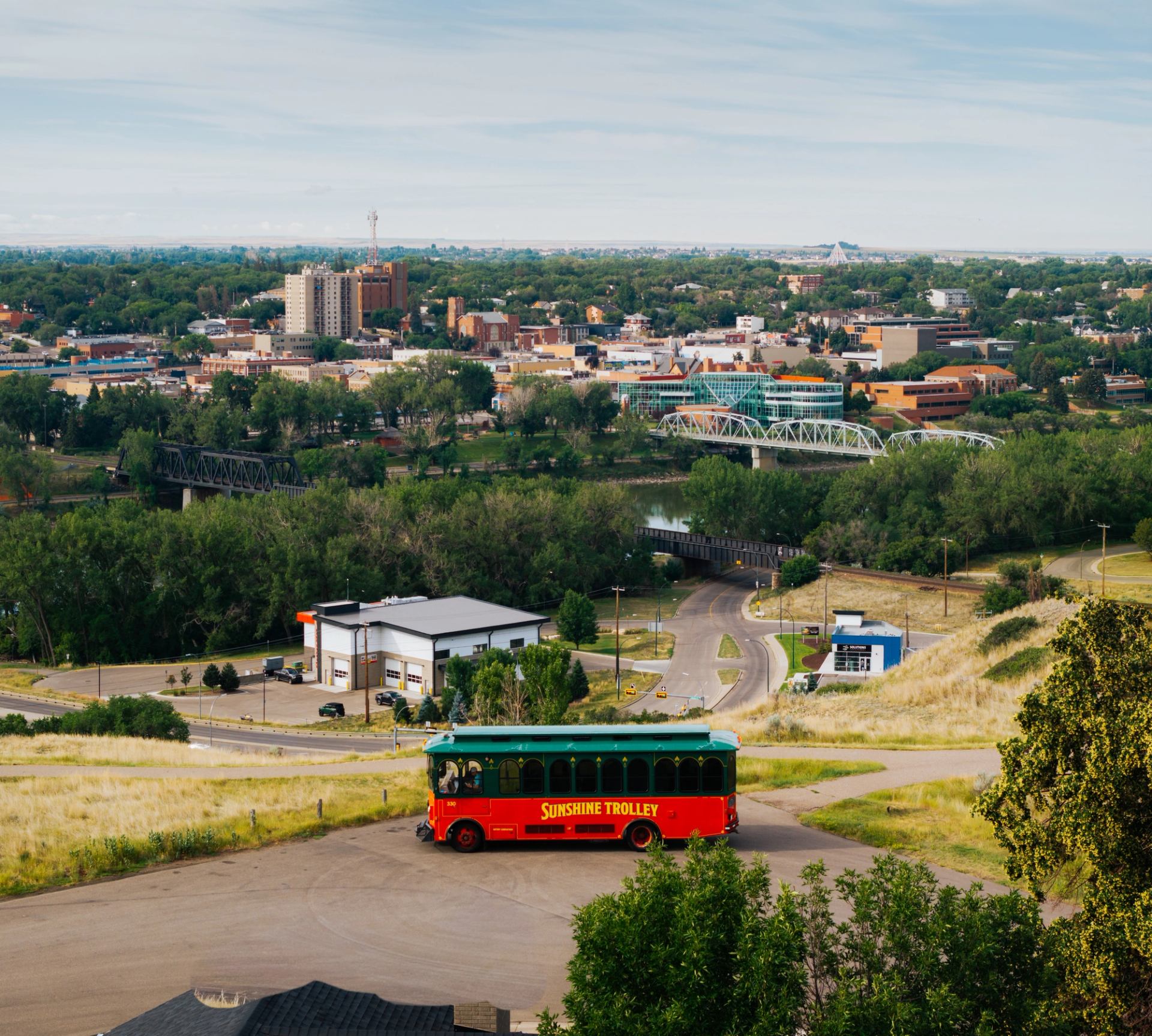 Red Sunshine Trolley bus on hillside road overlooking river, bridges and city buildings.