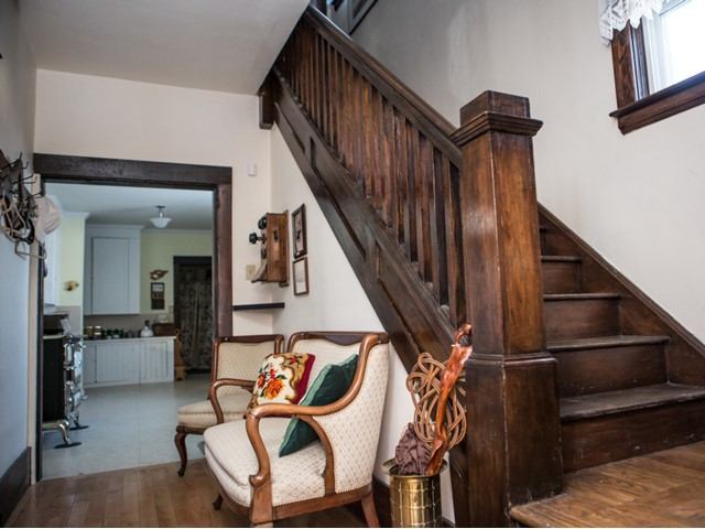 Wooden staircase beside upholstered chairs and doorway leading to a kitchen.