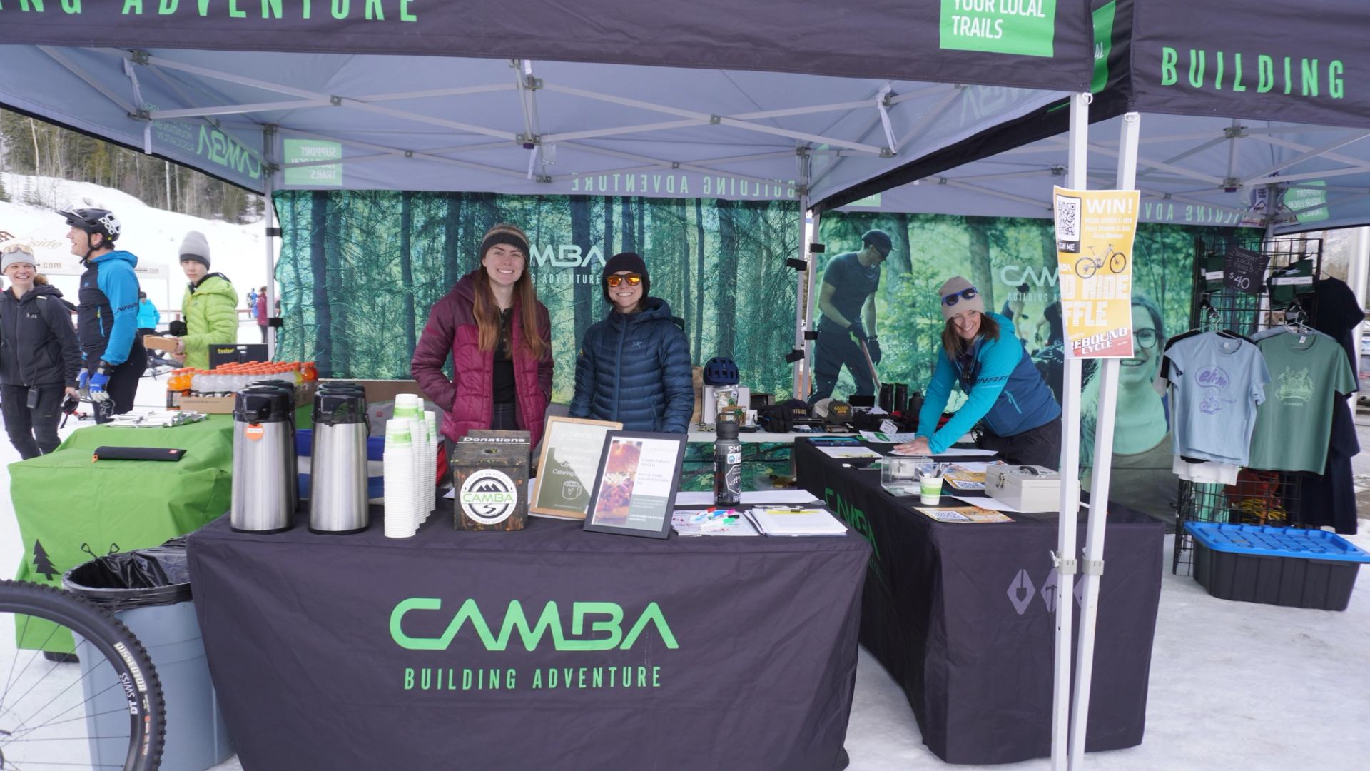 CAMBA booth at an outdoor winter event with staff, gear displays, and merchandise under tents.