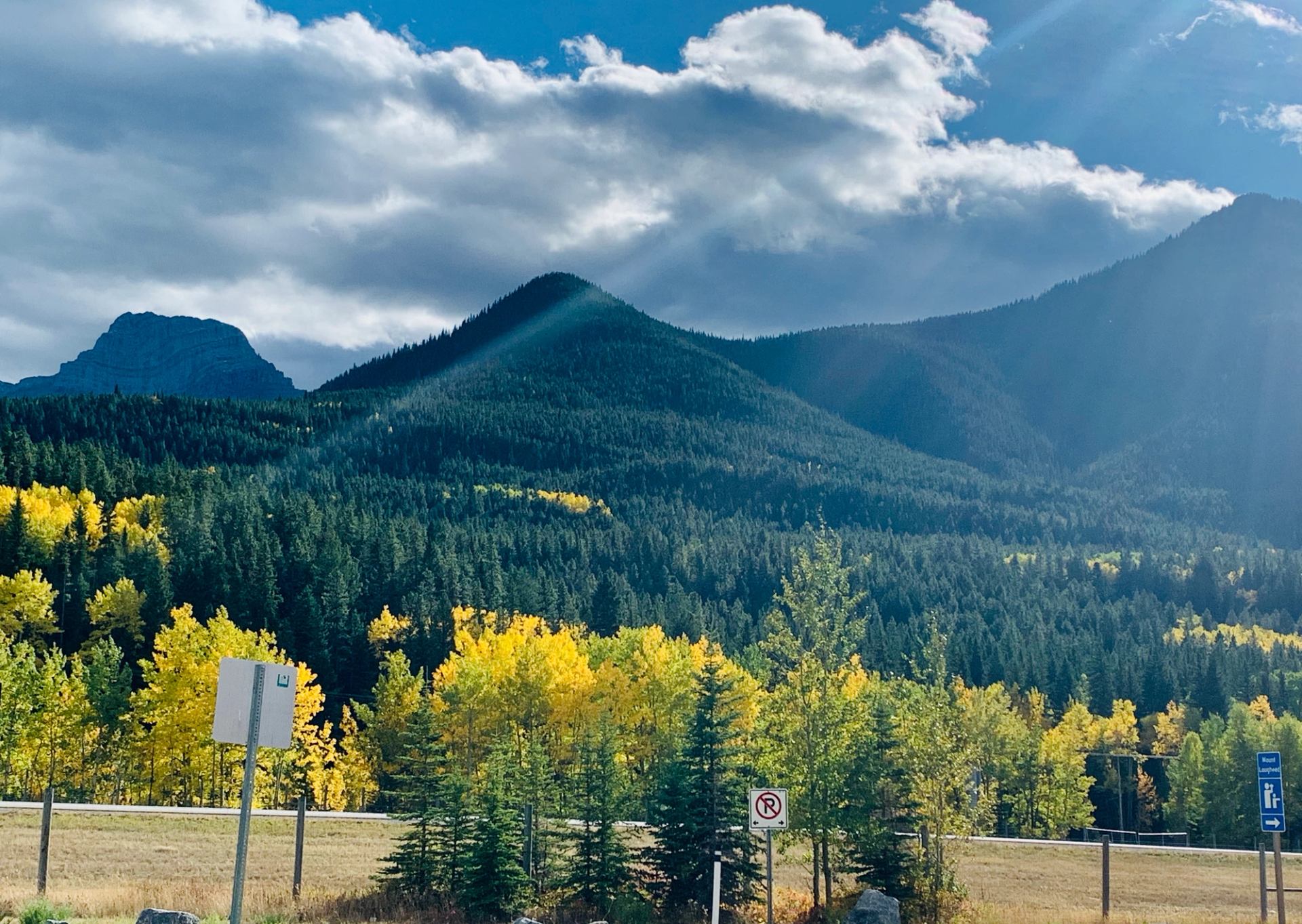 Autumn mountains with vibrant yellow trees and sun rays breaking through clouds.