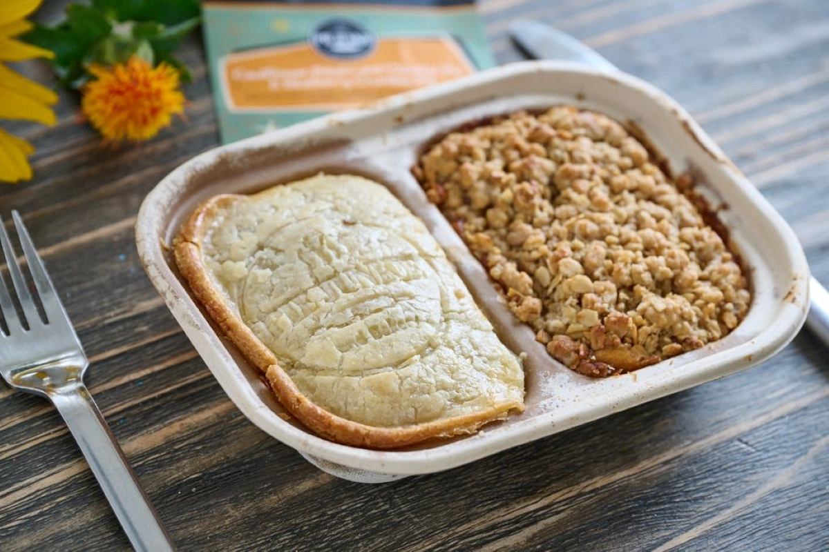 Baked savoury pie and apple crumble served together in a divided tray on a wooden table.