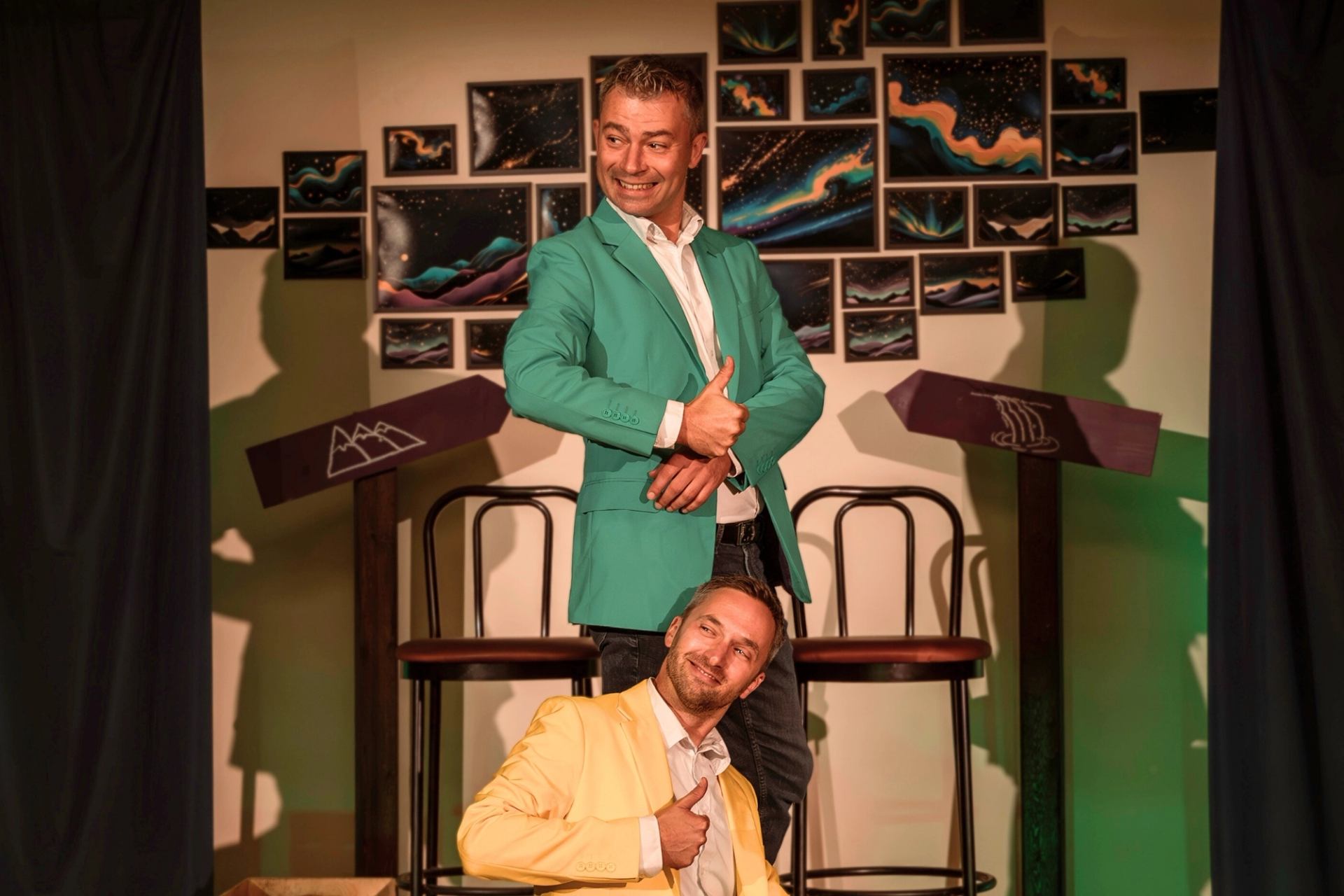 Two performers posing onstage with colorful art behind them
