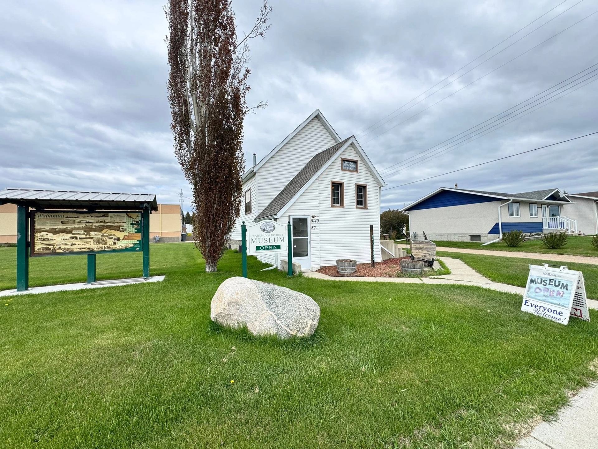 Museum building surrounded by green lawn, interpretive signage, and trees beneath cloudy skies.