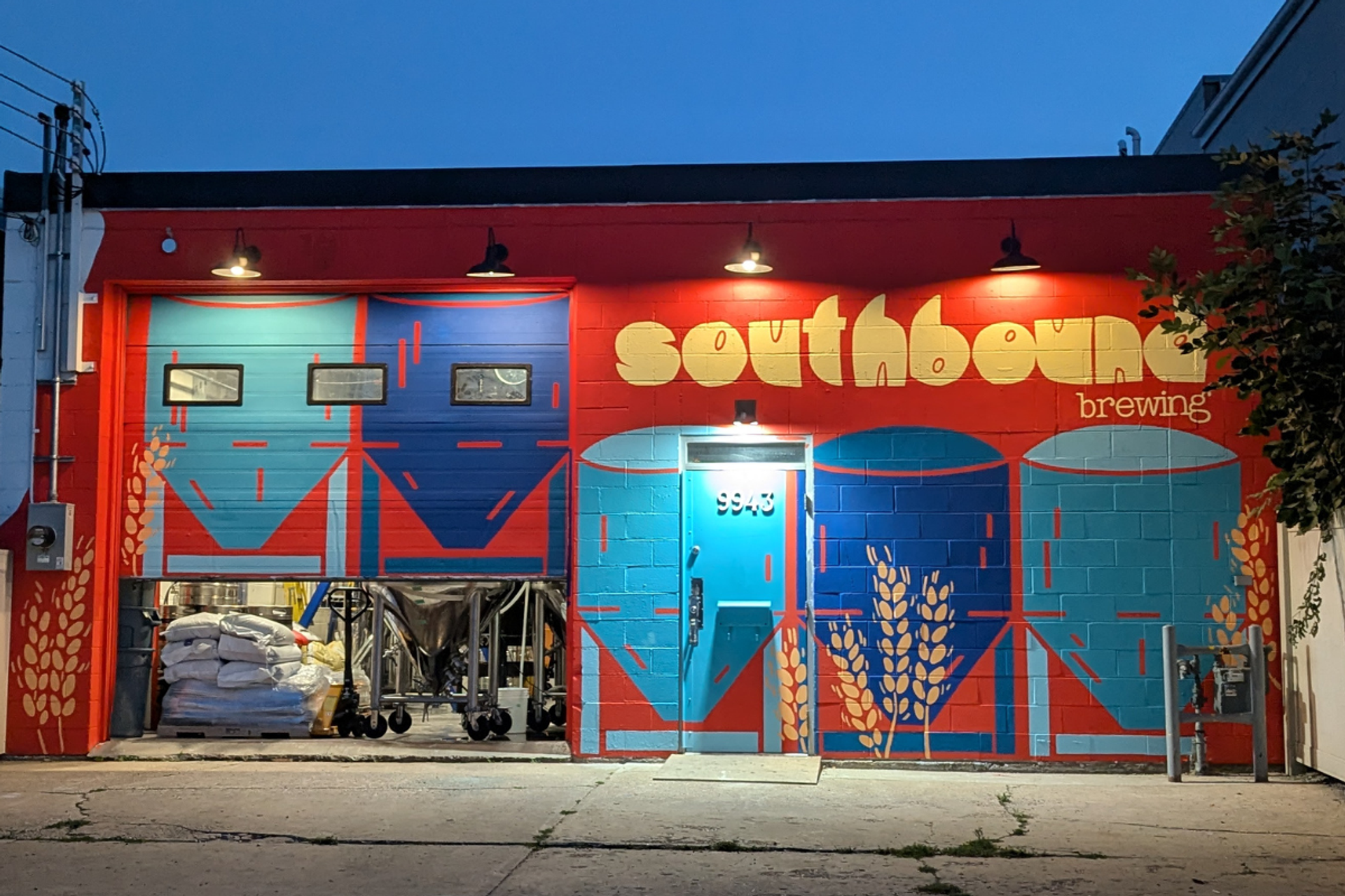 Colorful mural with tanks and wheat at Southbound Brewing during twilight.