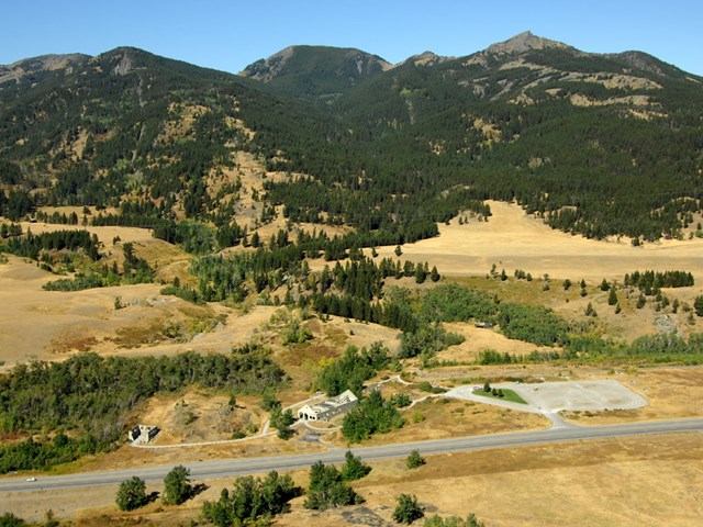 Mountain landscape with forested slopes, open fields, and a road under a clear blue sky near Leitch Collieries.