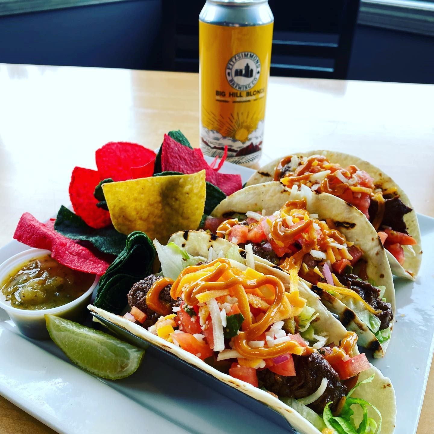 Plate of tacos with colorful chips, lime wedges, salsa, and a craft beer can.