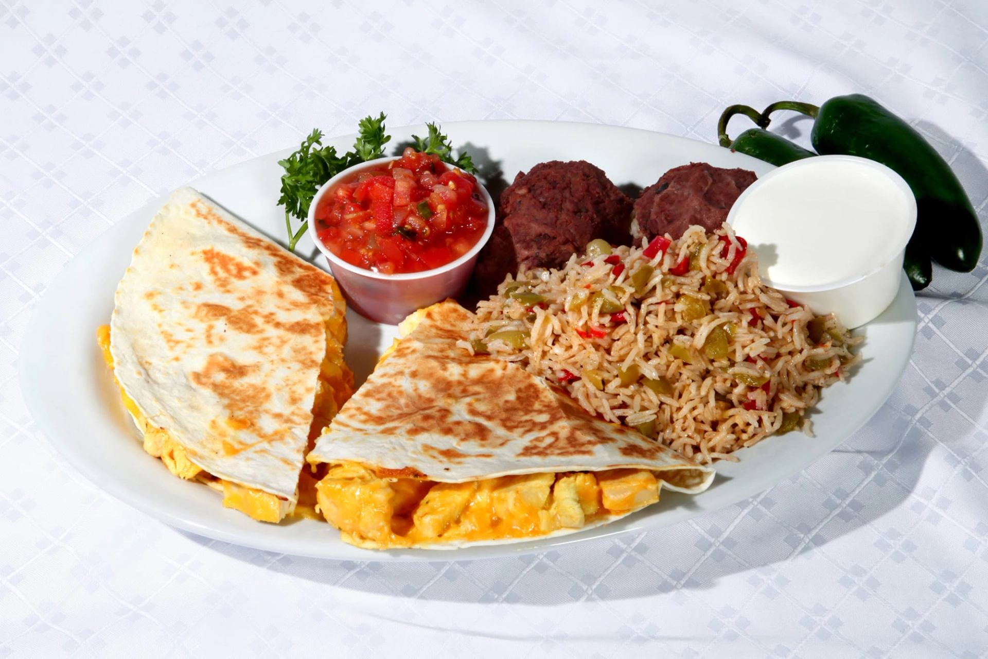 A grilled quesadilla is served with rice, refried beans, fresh salsa, and a sour cream.