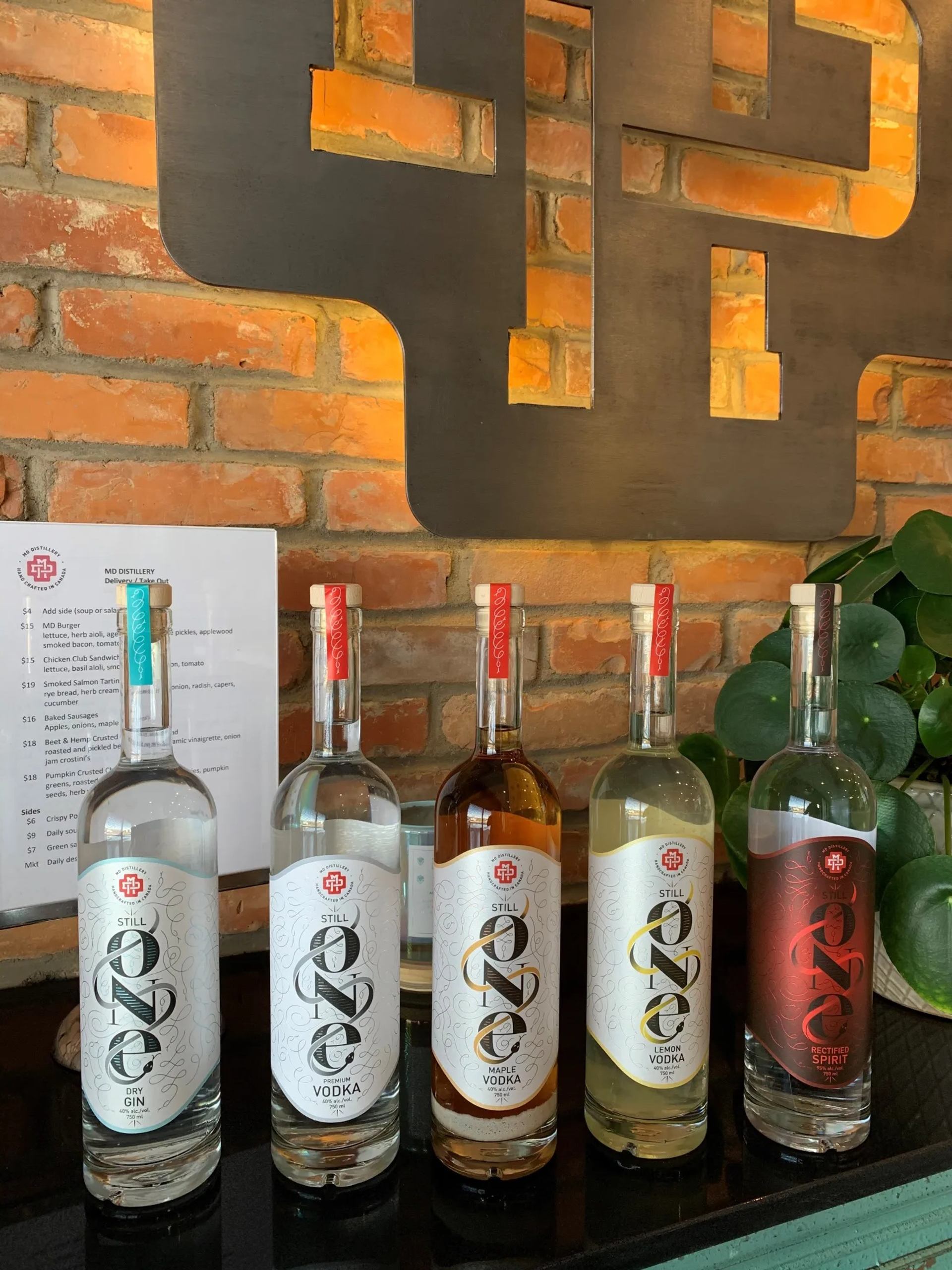Five Still Spirits liquor bottles on a bar counter against a brick wall backdrop.