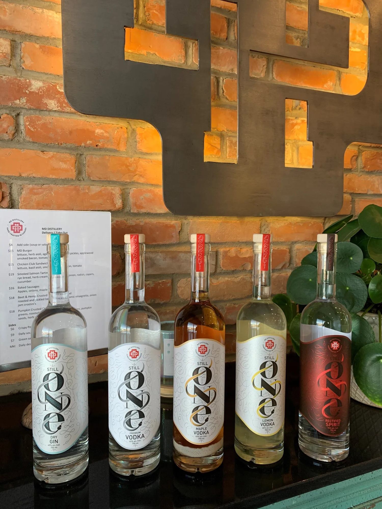 Five Still Spirits liquor bottles on a bar counter against a brick wall backdrop.