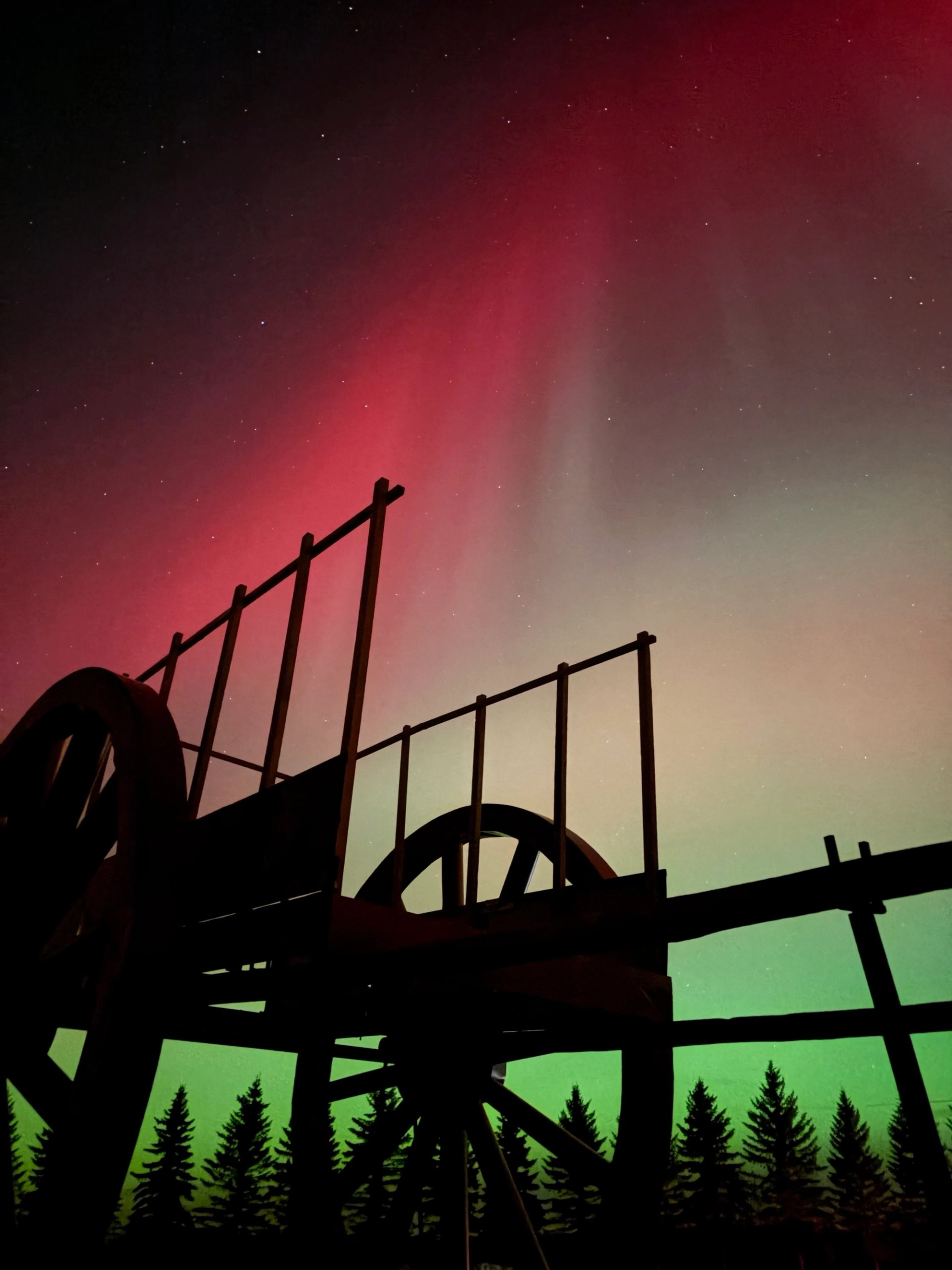 Silhouette of Alberta’s Largest Red River Cart under glowing red and green northern lights.