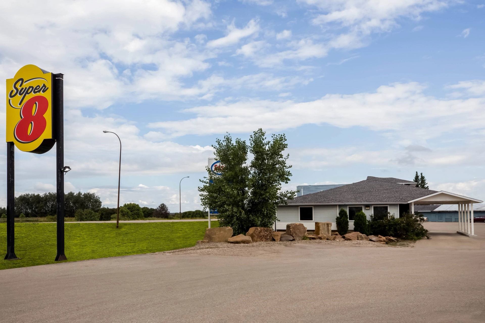 A Super 8 motel with a large sign in the foreground, a small building, and a grassy area with trees.