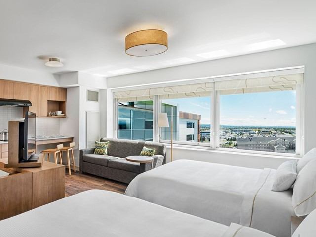 Modern hotel room with beds, sofa, kitchenette, and city view at Element Calgary Airport.