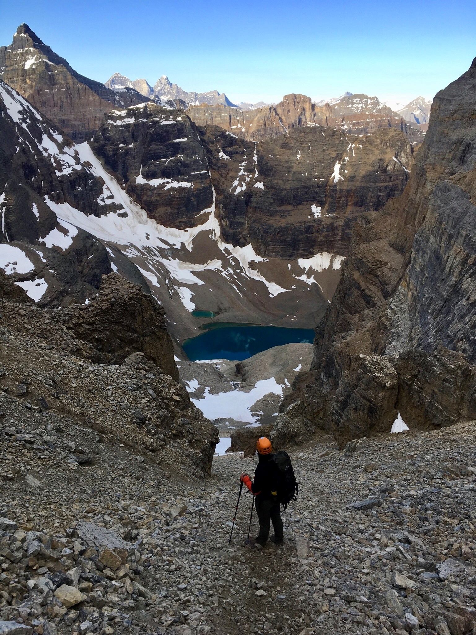 Hiker on rocky trail overlooking lake and snowy peaks.