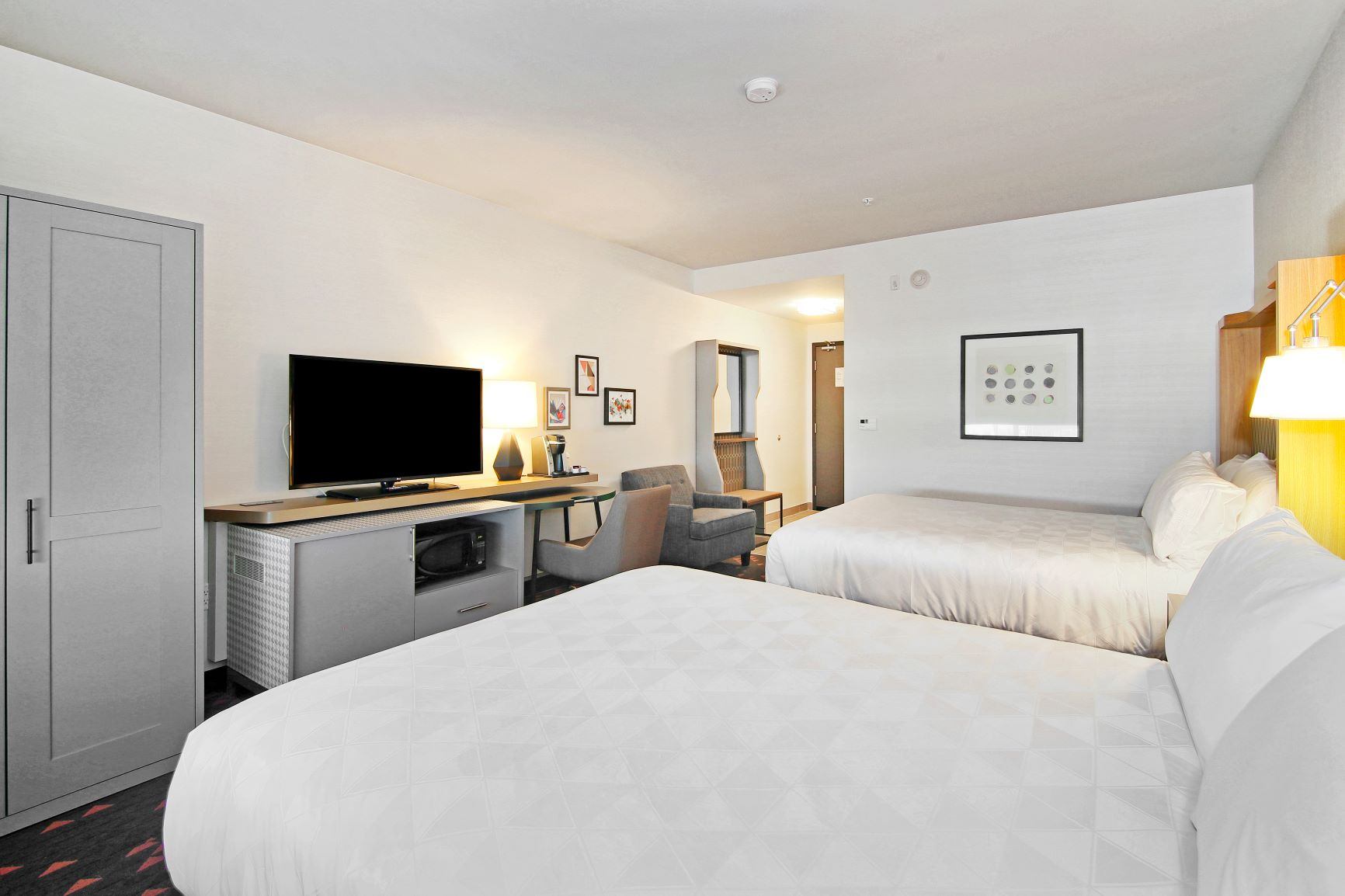 Modern guest room with two queen beds, TV, desk, and bright lighting