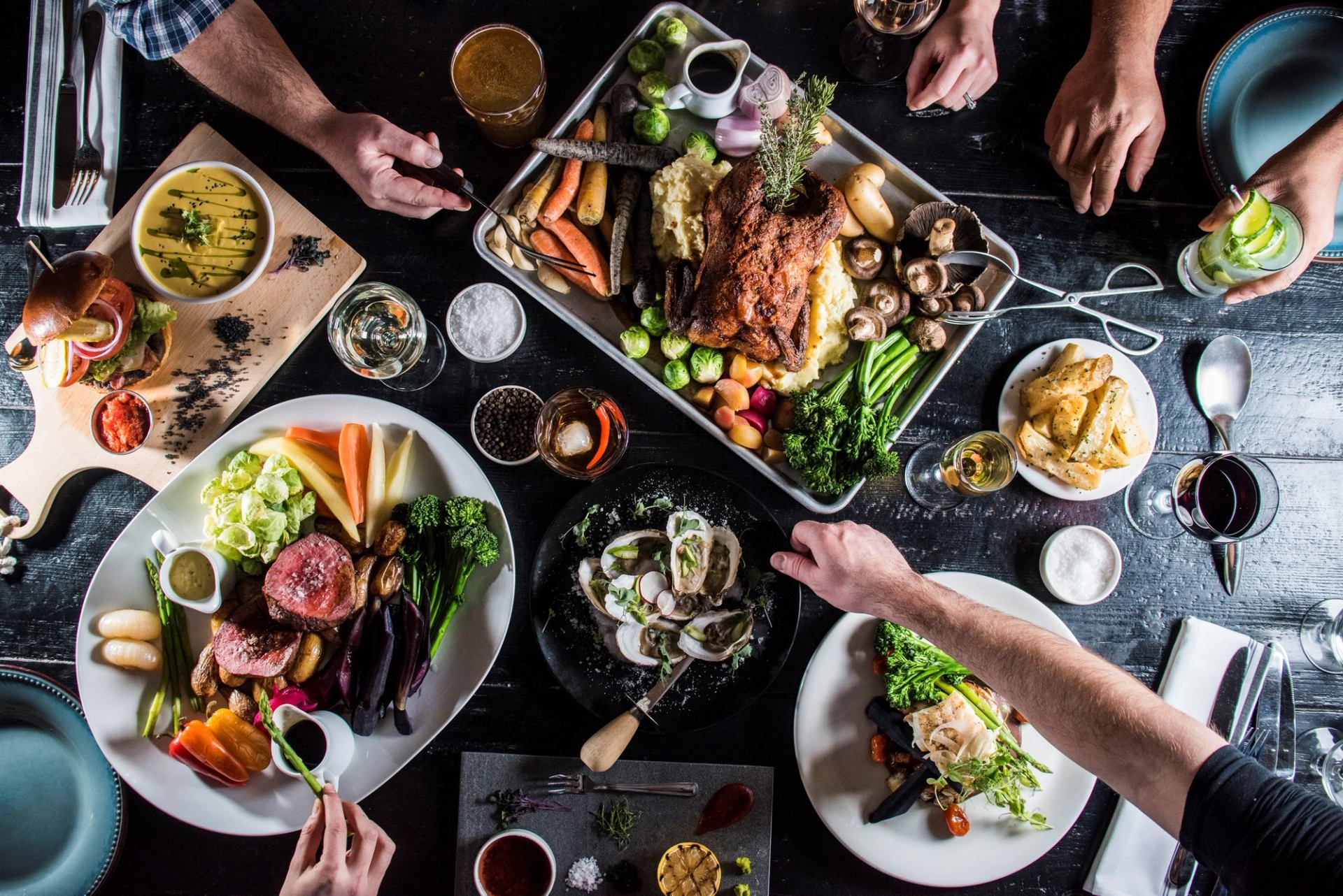 Top-down view of shared meal with meats, seafood, salads, and drinks.