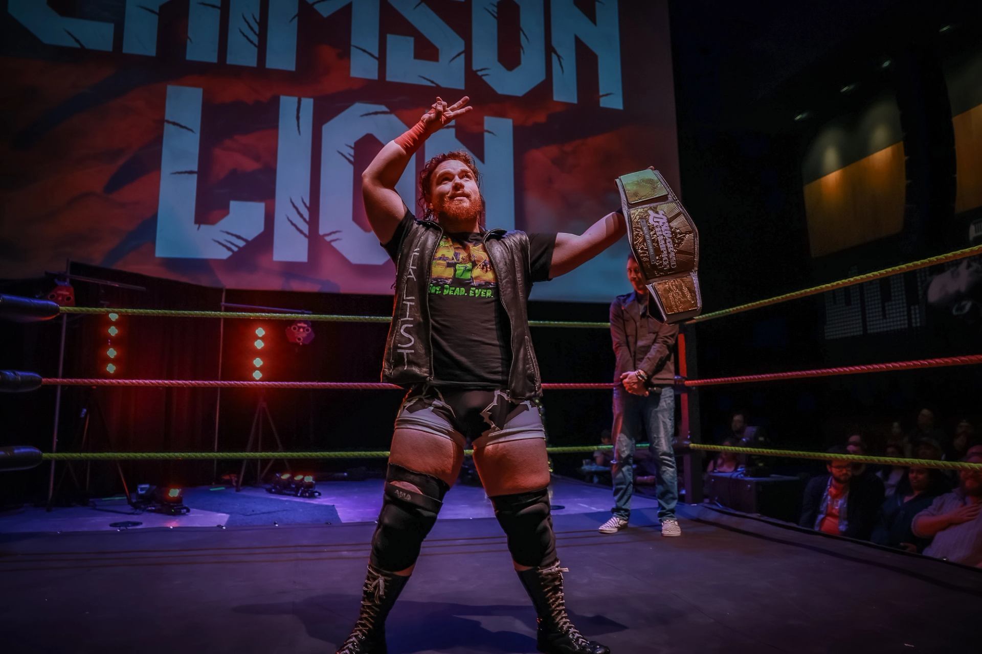 Wrestler stands in the ring holding a title belt with Love Pro Wrestling signage behind.