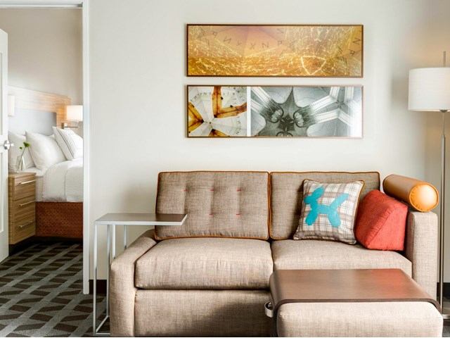 TownePlace Suites living area with sofa, artwork, and view into bedroom.