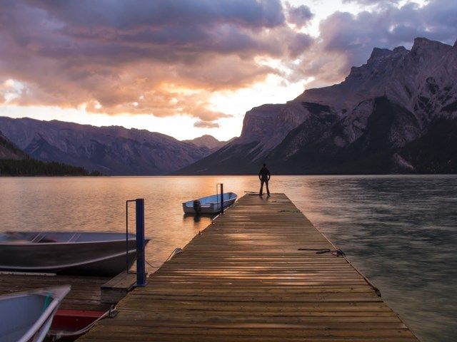 Man standing at the end of the dock at Lake Minnewanka at dusk.