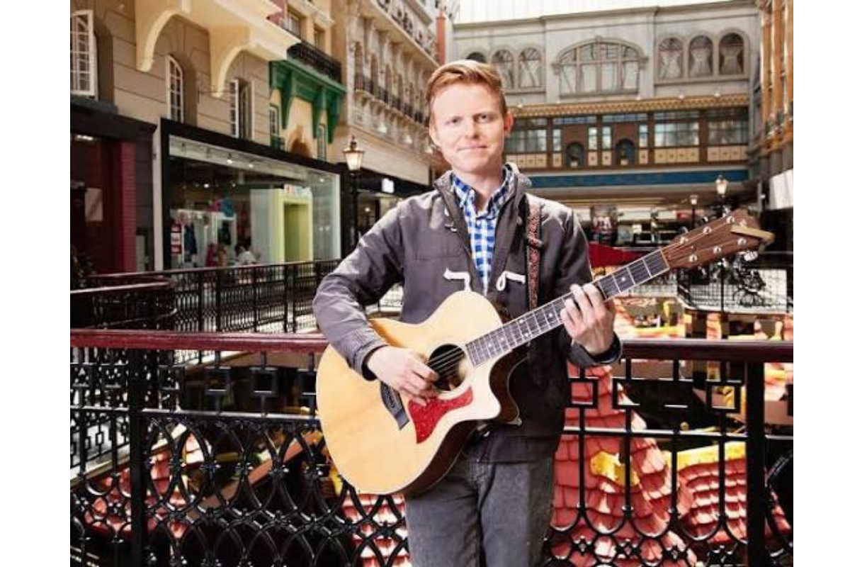 Guitarist plays an acoustic guitar inside an ornate multi-level shopping centre.