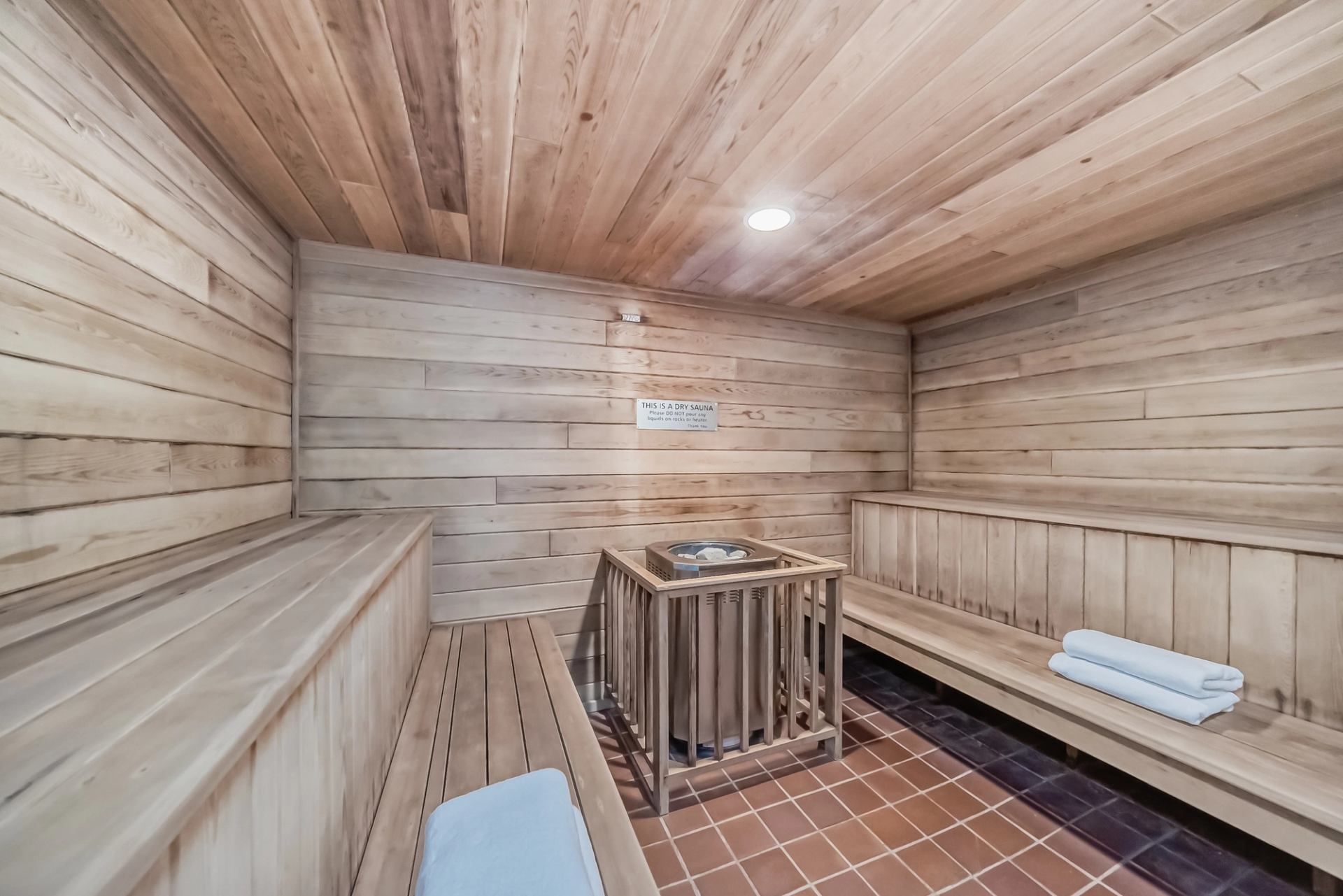 Interior of a wooden sauna with benches, heater, and folded towels on the seating area