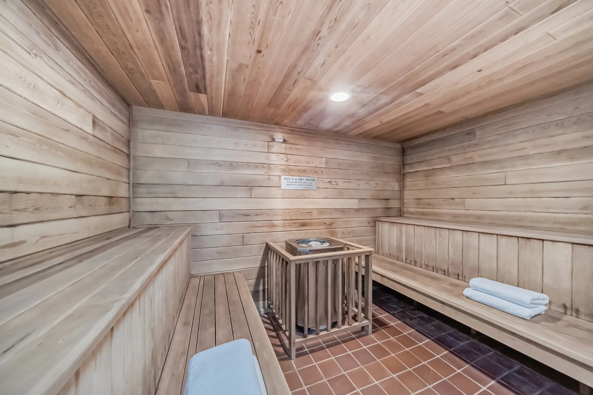 Interior of a wooden sauna with benches, heater, and folded towels on the seating area