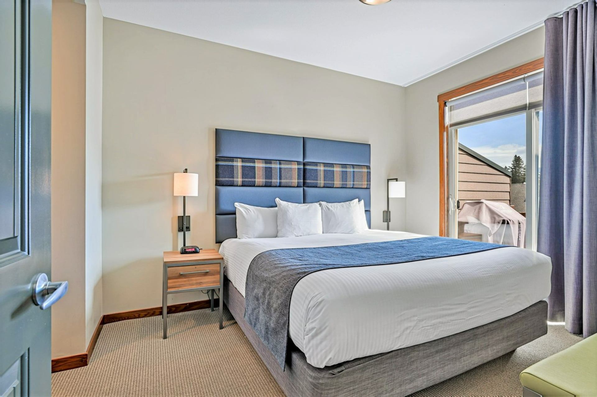Bedroom with a large bed, blue headboard, bedside lamps and balcony door.