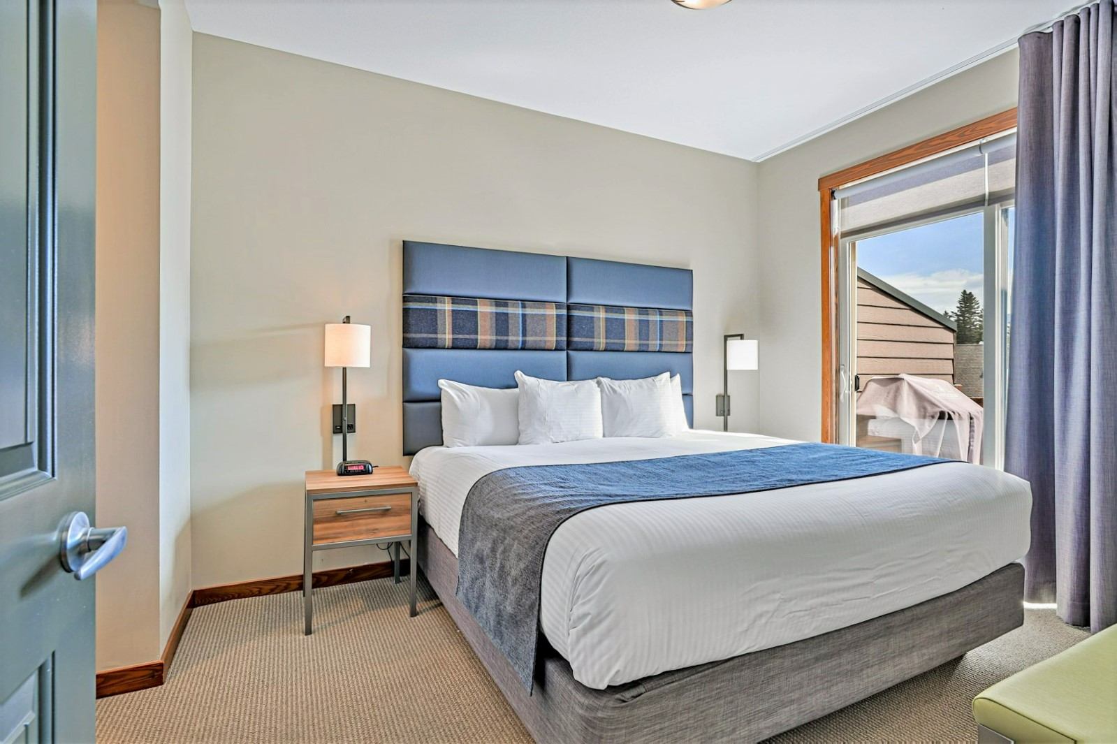 Bedroom with a large bed, blue headboard, bedside lamps and balcony door.