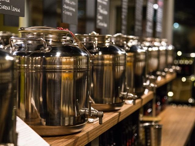 Row of shiny metal dispensers on a wooden shelf in a store setting.