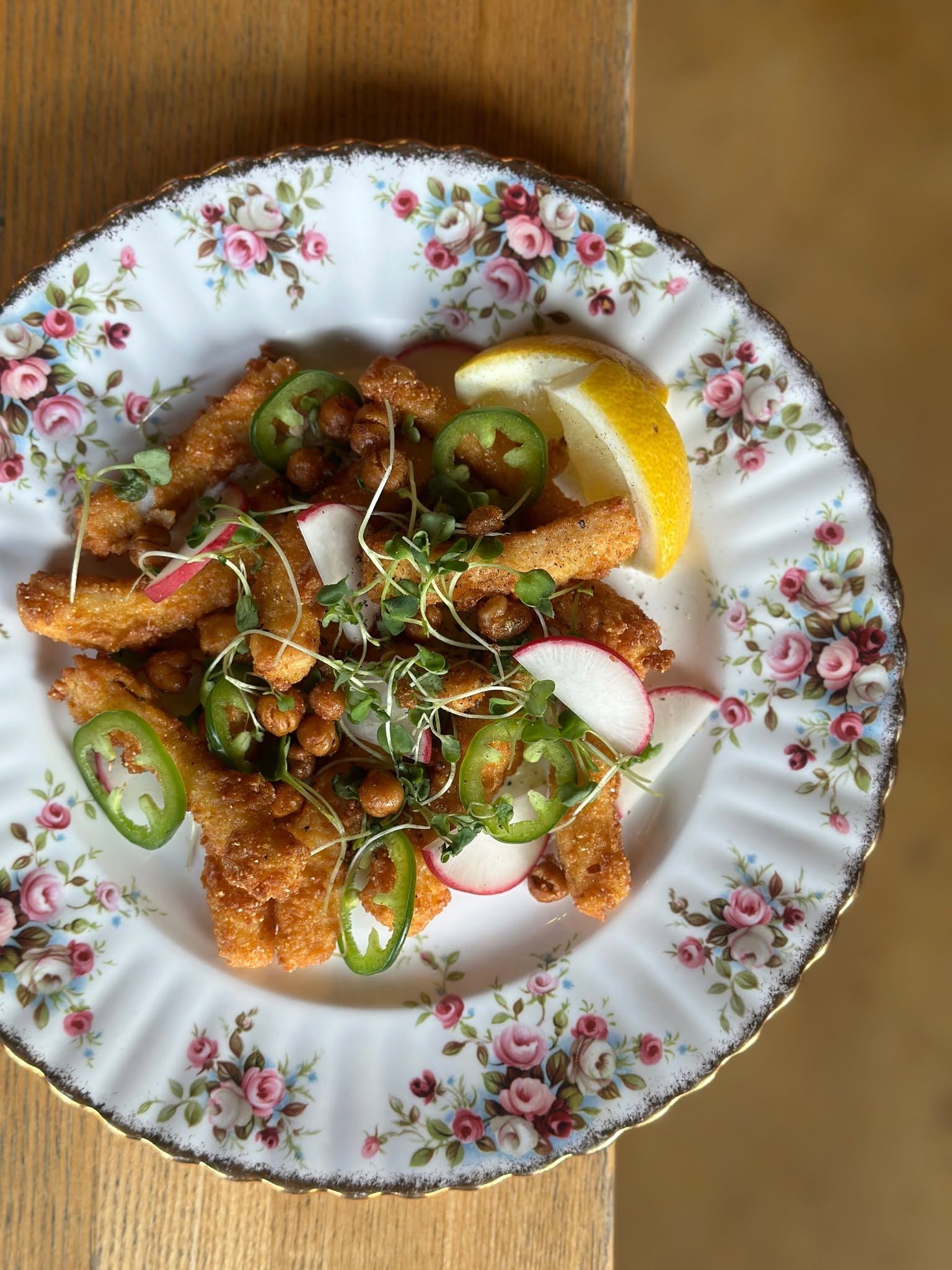 Crispy fried bites are topped with jalapeños, radish slices, sprouts, and a lemon wedge.