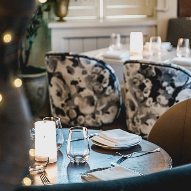 Round table set with glasses, napkins, and candles in a warmly lit restaurant interior