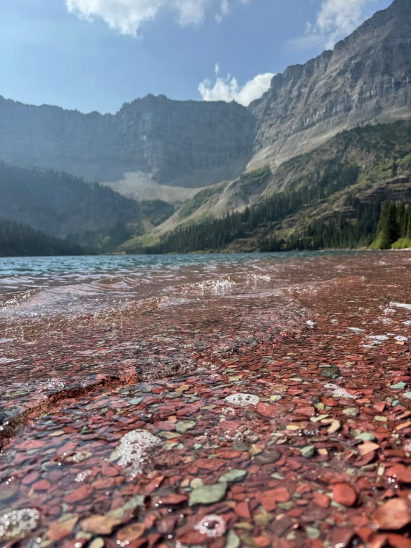 Clear lake with red pebbles in foreground and rugged mountains in Bertha Lake.