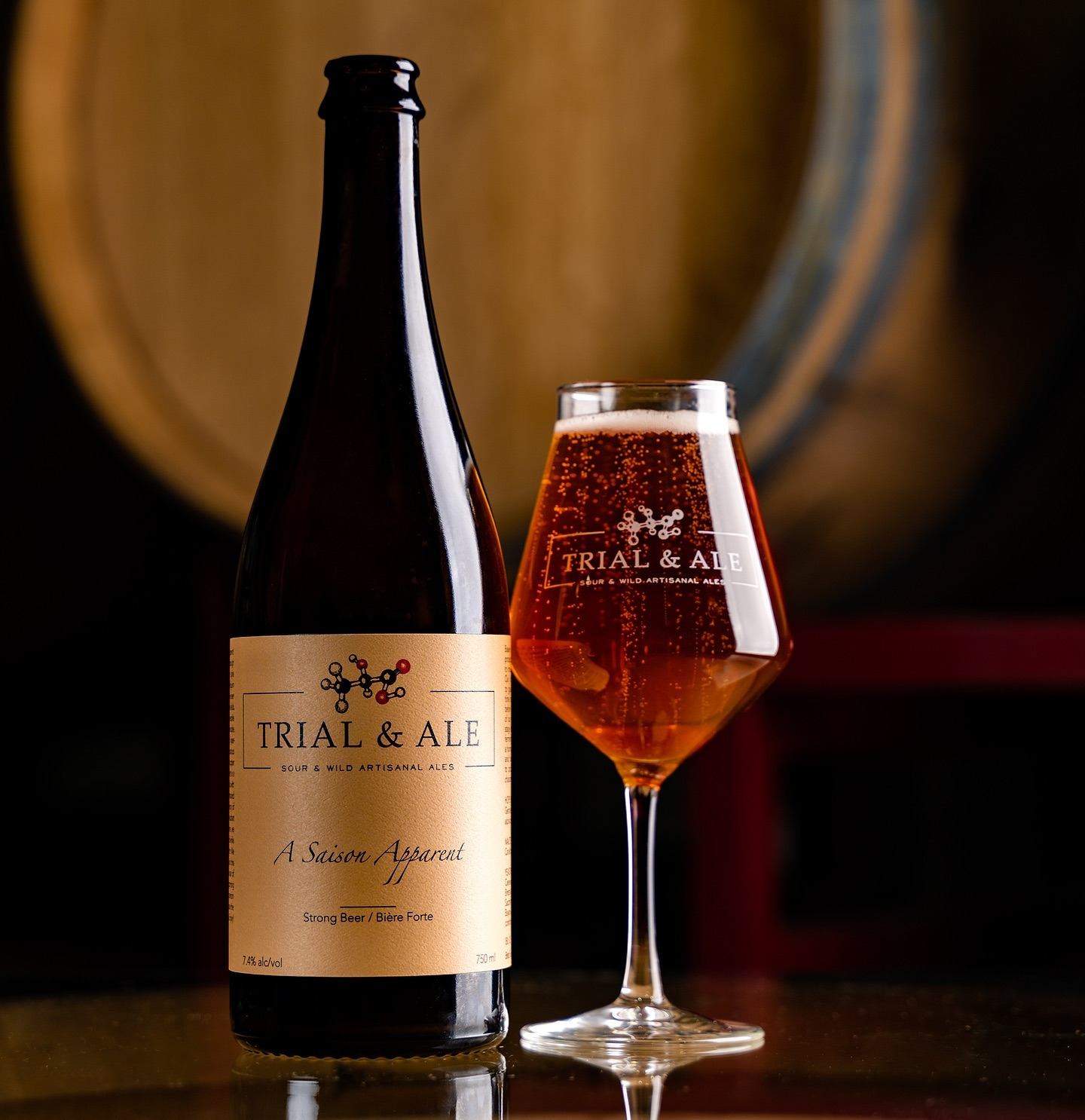 Bottle of Trial & Ale saison beside a filled branded glass on a table.