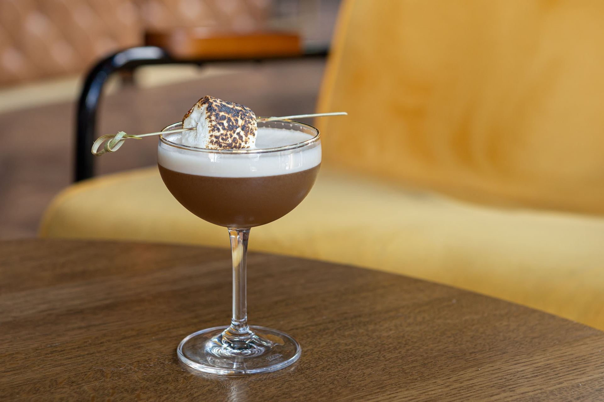 Dark cocktail topped with foam and toasted marshmallow garnish