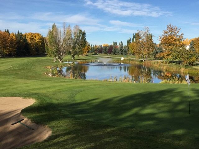 Beautiful golf course in autumn, featuring a pond with a fountain, surrounded by trees with fall foliage.