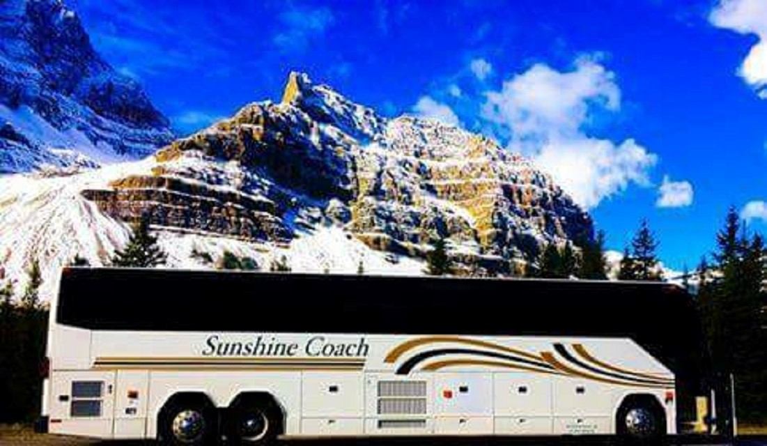 Sunshine Coach bus parked with snowy mountains and blue sky in the background.