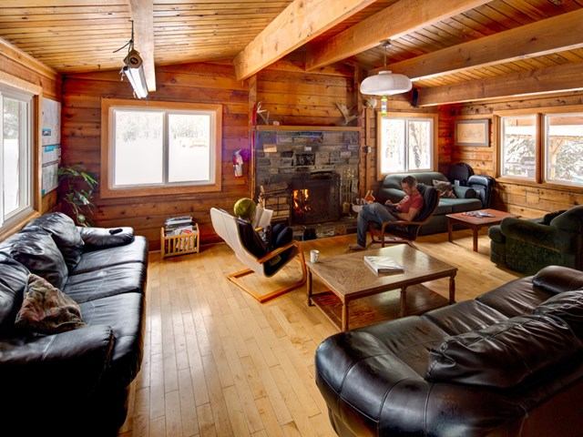 Rustic lounge with leather couches, stone fireplace, and wood-paneled walls.