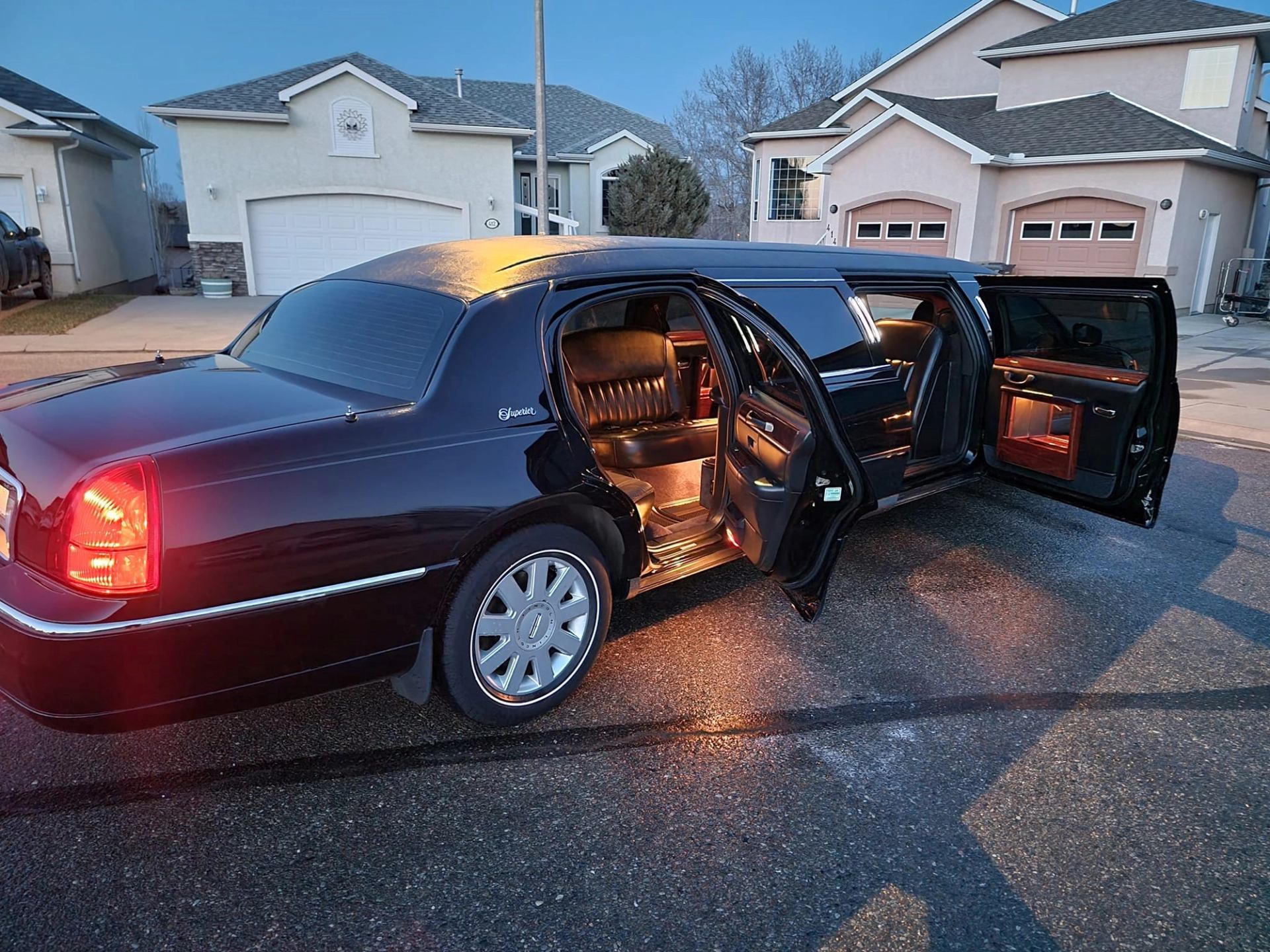 Black stretch limo with open doors and lit interior parked on a residential street.
