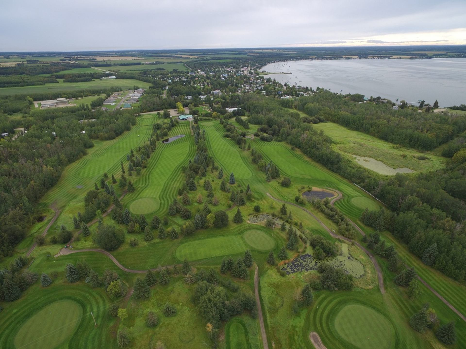 Aerial view of a green golf course beside a lakeside town and surrounding farmland.