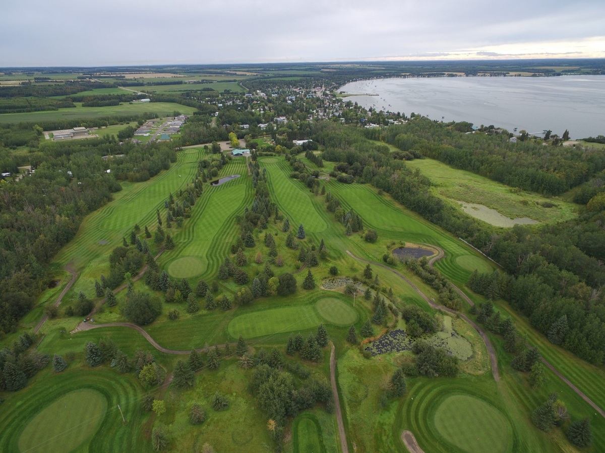 Aerial view of a green golf course beside a lakeside town and surrounding farmland.