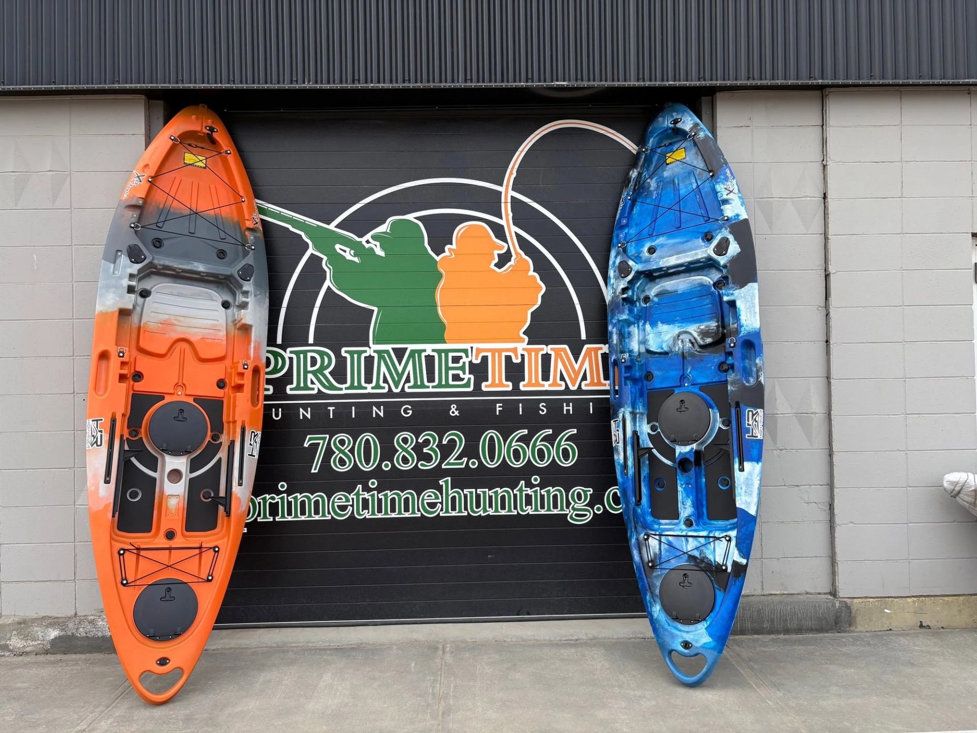 Orange and blue kayaks lean against a Prime Time Hunting & Fishing garage door.