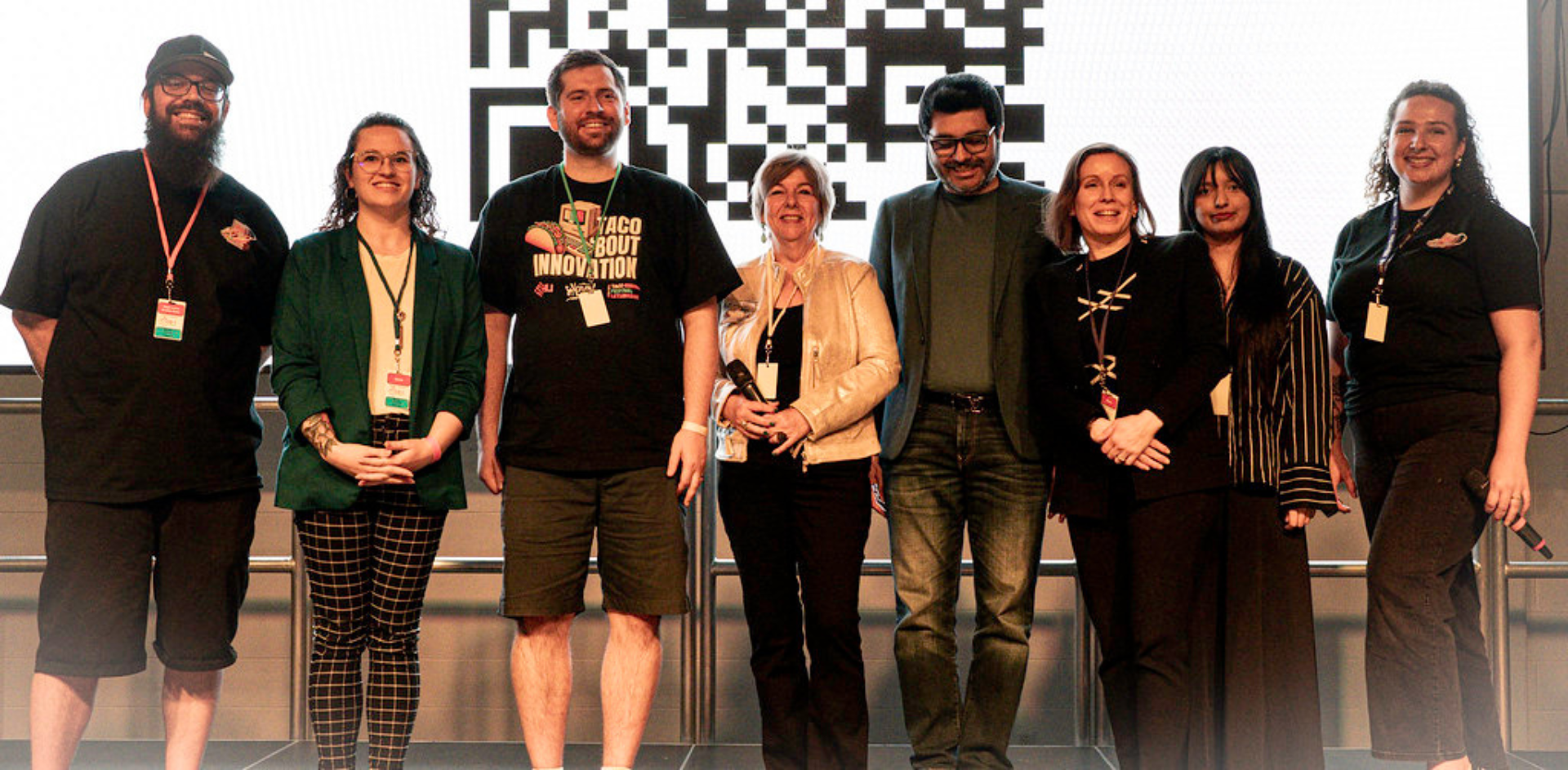 Group of people standing on stage in front of a large screen displaying a QR code. 